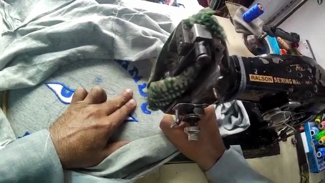 Raw frame 150 of the reference clip, from the wearer's viewpoint: the left hand aligns and organizes fabric items on a workstation surface beside a sewing machine — the action the published annotation records for this segment.